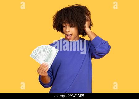 Excited young man holding money against a bright yellow background Stock Photo
