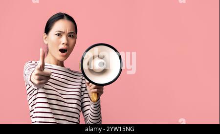 Attention. Emotional Asian Lady With MLoudspeaker Shouting And Pointing Finger At Camera Stock Photo