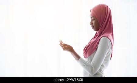 Portrait of young black muslim woman praying near window at home Stock Photo