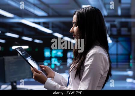 Engineer in data center updating systems to keeps performance up and protect servers from easily exploitable software vulnerabilities. Employee looking for errors causing servers to slow down using tablet Stock Photo