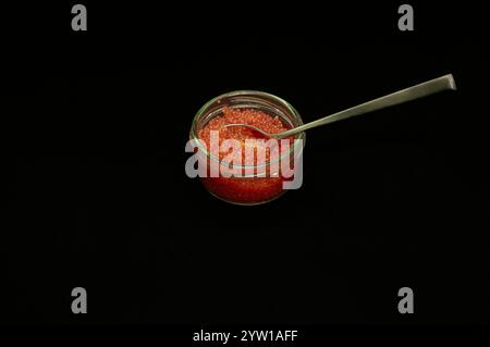 red lumpfish roe and a spoon in a glass jar isolated on black Stock Photo