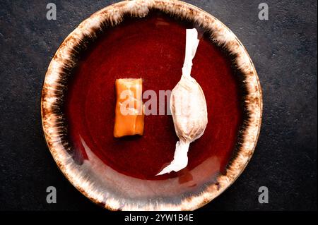 Top view of two homemade caramel candies, one wrapped in paper, on a rustic brown plate Stock Photo