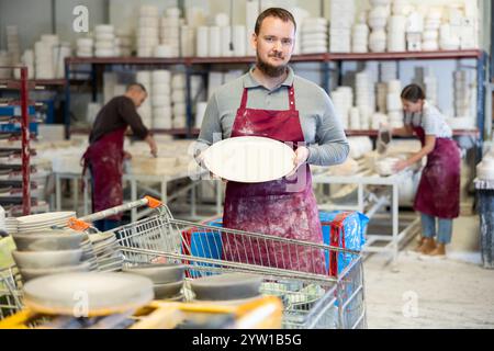 Successful potter displaying handcrafted plate in artisanal pottery studio Stock Photo