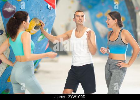 Athletic man and two sporty women discussing climbing options near climbing wall Stock Photo