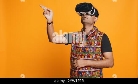 Indian man wearing virtual reality headset, doing swiping gestures. Technology enthusiast using high tech futuristic modern VR gadget, isolated over studio background, camera B Stock Photo