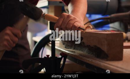 Experienced woodworker shaping raw timber using chisel and hammer, enjoying diy hobby. Woodworking professional in studio shaping wooden pieces with tools, making wood sculptures, camera A close up Stock Photo