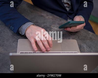 Businessman working remotely at a modern office desk, using a laptop and holding a smartphone, effectively managing tasks and maintaining Stock Photo