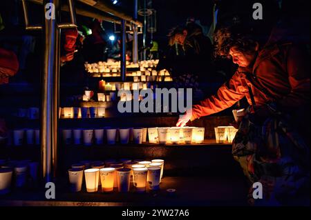 Nijmegen, Netherlands. 08th Dec, 2024. People light candles inside of paper cups on a windy night to commemorate World Candle Day. Around 18,000 candles were lit to remember all deceased children in the Palestine-Israel-Lebanon region. The candles were placed along the stairs leading to the quay on the Waal in Nijmegen. At the same time, the names of the children who died in the war in the past year were read by people attending the event. Credit: SOPA Images Limited/Alamy Live News Stock Photo