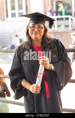 Smiling woman in graduation gown and cap holding a diploma with a red ribbon, Bournemouth, Dorset UK Stock Photo