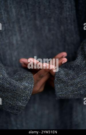 A close-up of folded hands behind a person's back, set against a textured gray woolen coat, Brandenburg, Germany Stock Photo