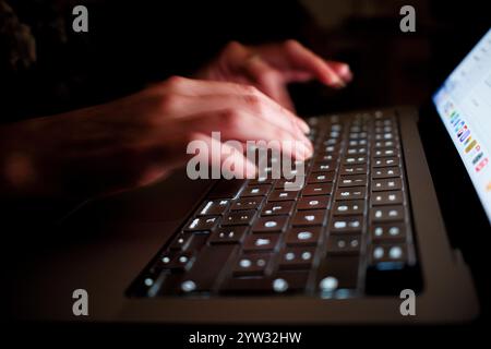 Close-up of hands typing on a backlit laptop keyboard in low light conditions. Stock Photo