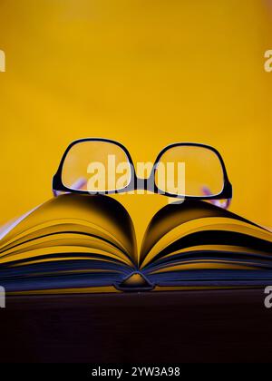 Reading Glasses on Top of an Open Book - Yellow Background Stock Photo