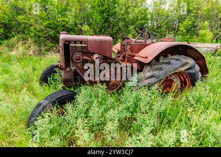 An old tractor is sitting in a field of grass. The tractor is rusted and has a worn appearance. The grass is tall and green, and the tractor is surrou Stock Photo