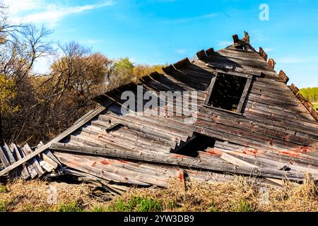 A dilapidated old wooden building with a triangular roof. The roof is missing several pieces and the building appears to be in a state of disrepair Stock Photo