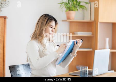 Young woman taking notes from a laptop at a modern workspace. Stock Photo