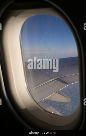 Airplane wing and clouds viewed through an aircraft window during flight. Stock Photo