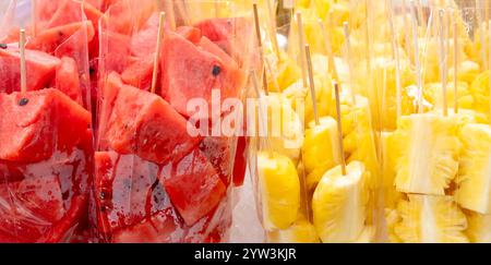 Full frame of red watermelon and yellow pineapple in pieces or slices in transparent plastic bag are on sale at street food stall. Stock Photo