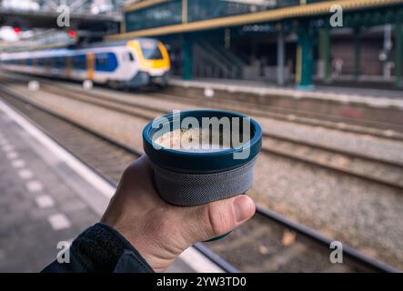 Enjoying Coffee To Go at Dutch Train Station, Holding a Reusable and Foldable Plastic Cup of Cappuccino While Waiting for the Train Stock Photo