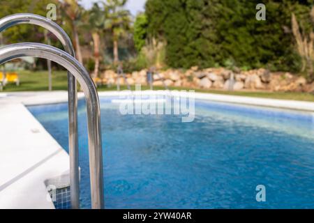 Photo of a beautiful swimming pool in the summer time showing the empty pool and metal steps leading in the pool with yellow sun loungers and palm tre Stock Photo