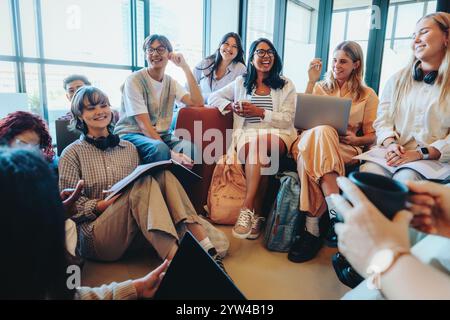 A group of diverse students in a casual classroom setting, engaging with laptops and study materials. They are sharing ideas and enjoying a collaborat Stock Photo