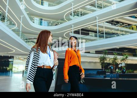 Two professional women conversing in a contemporary business environment, highlighting career growth in the finance industry. Stock Photo