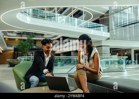 Two young professionals are engaged in a lively corporate meeting in a modern office setting. They appear to be discussing a project on a laptop, show Stock Photo