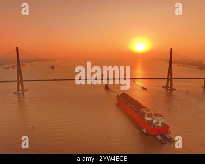 (241209) -- NANJING, Dec. 9, 2024 (Xinhua) -- This aerial drone photo taken on Dec. 9, 2024 shows the 'NGUYA FLNG,' a floating liquified natural gas (FLNG) facility, being tugged through the Sutong (Suzhou-Nantong) Bridge across the Yangtze River in east China's Jiangsu Province. The 'NGUYA FLNG,' the first large-scale FLNG facility made in the country, was transferred from Nantong of Jiangsu to Zhoushan of Zhejiang (both in east China), where it will be further assembled, integrated and modulated. An FLNG facility is capable of directly liquifying and storing natural gas harvested from an o Stock Photo