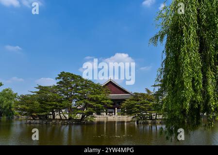 A pond with a red building in the background. The building is a house. The pond is surrounded by trees Stock Photo