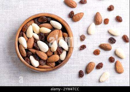 Student food, a trail mix in a wooden bowl, on linen fabric. Mixture of almonds with seed coats and blanched, and of raisins Stock Photo