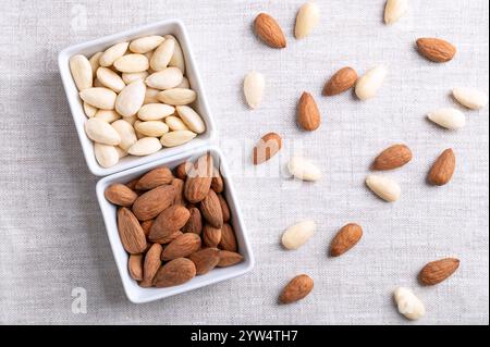 Almonds in square shaped white bowls, on linen fabric. Almonds with seed coats and blanched. Stock Photo