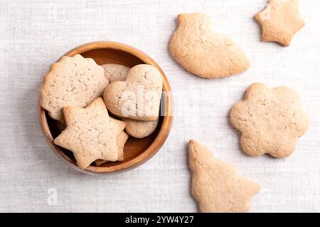 Homemade gingerbread cookies in a wooden bowl on linen fabric. Sweet, light brown and flat baked goods for Christmas season. Stock Photo