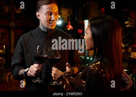 A young couple shares a joyful moment over glasses of wine at a lively bar. Stock Photo