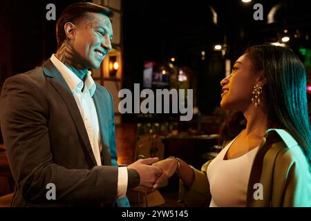 Tattooed man smiles while holding hands with a beautiful woman during their night out. Stock Photo