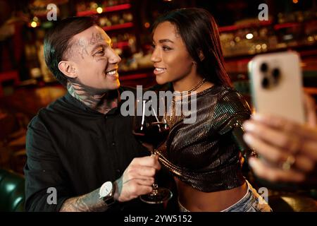 Tattooed man and woman share an intimate moment while enjoying drinks at a lively bar. Stock Photo