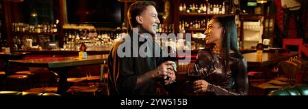 Tattooed man and woman share a romantic night out, holding glasses of wine in a lively bar setting. Stock Photo
