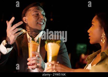 Young multicultural couple shares laughter and drinks on a lively evening date. Stock Photo
