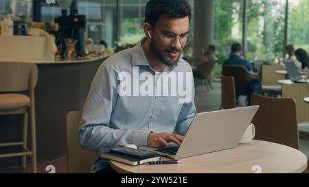 Arabian Indian man typing laptop keyboard concentrated business guy male businessman at cafe table online work computer browsing internet write tasks Stock Photo