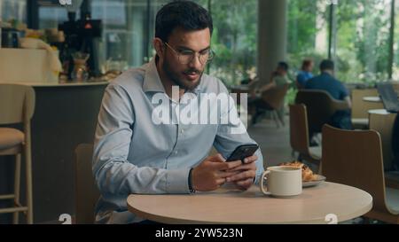 Arabian man ethnic muslim Indian businessman guy entrepreneur manager using mobile phone business lunch in cafe restaurant male visitor millennial Stock Photo