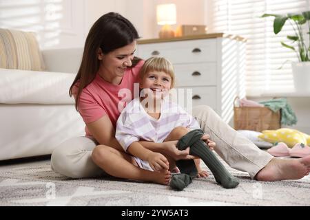 Mother helping her daughter to put tights on at home Stock Photo