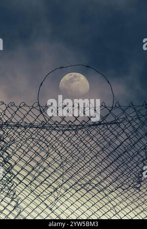 Full moon behind barbed wire fence. Stock Photo