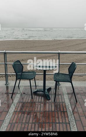 Wet tables and chairs at beach on a rainy day Stock Photo