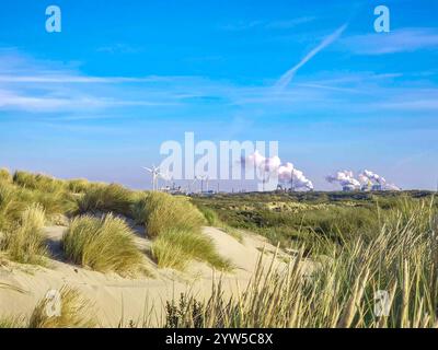 Dutch dune landscape near IJmuiden towards the blast furnaces in Velsen with smoking chimneys and water vapour and tall windmills to generate electric Stock Photo