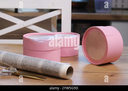 Three small gift boxes with windows. They are lying on the table. Next to them is a roll of kraft paper. A small pink box. Gift wrapping. Stock Photo