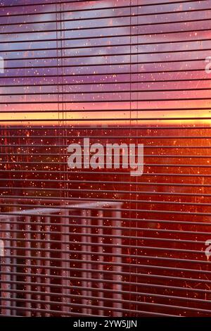 Sunset and rain through the window blindes and raindrops on window glass. Stock Photo