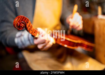 Violin maker working on a new violin in his workshop, varnishing the instrument with a brush Stock Photo
