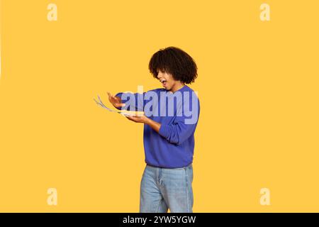 Young man with curly hair expressing excitement while engaging with money Stock Photo