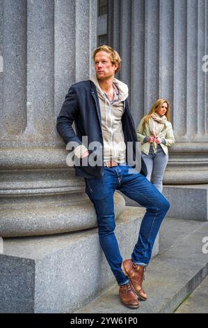 Two people are standing near large stone columns, with the man in the foreground leaning slightly against the structure and the woman in the backgroun Stock Photo