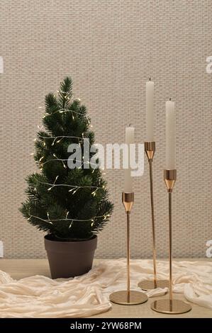 Christmas decor, tree with lights, candles in golden holder, beige cloth on wooden table Stock Photo