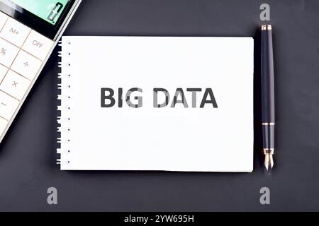 A notepad with the words big data prominently displayed sits on a desk alongside a calculator and pen, illustrating a focus on data analytics and tech Stock Photo