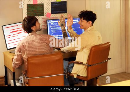 Male programmers giving each other high-five in office at night, back view Stock Photo